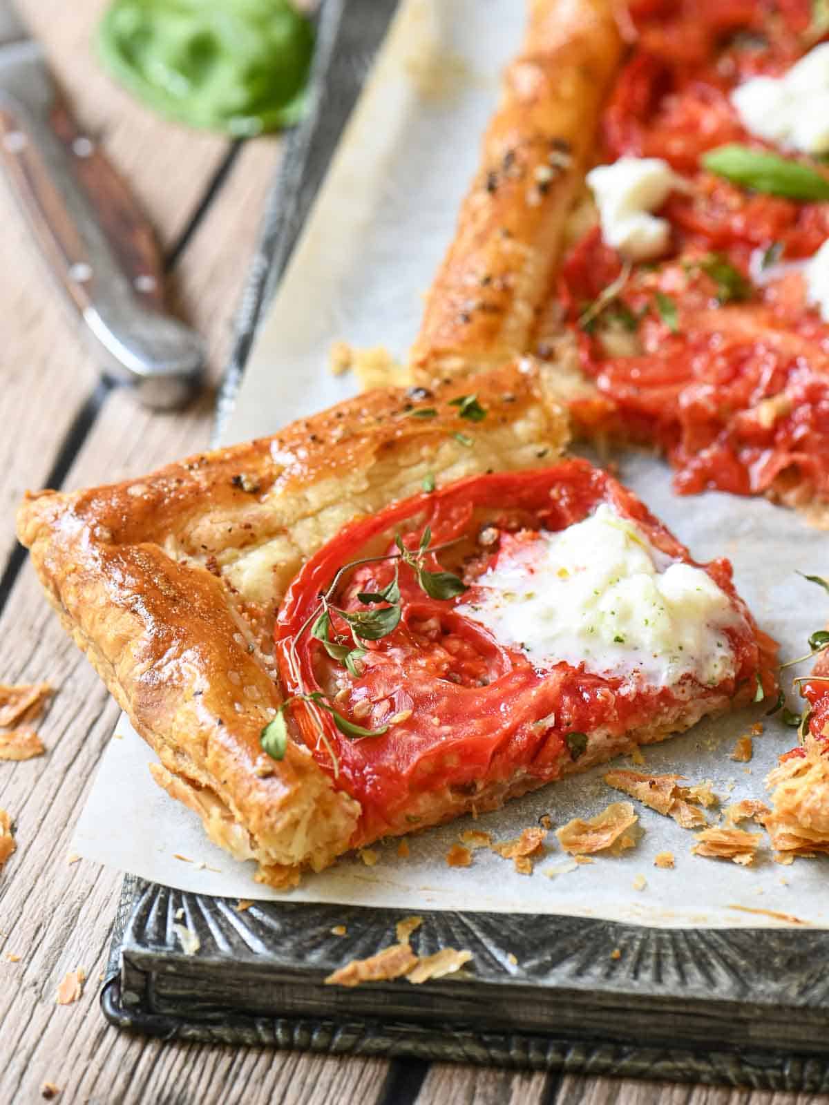 A slice of tomato tart with cheese cut out on a metal tray.