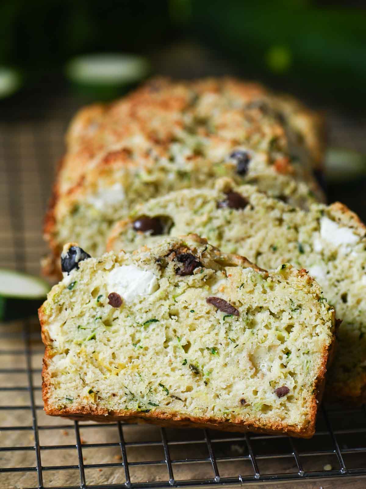 Savory zucchini bread slices leaning against each other on a metal rack.