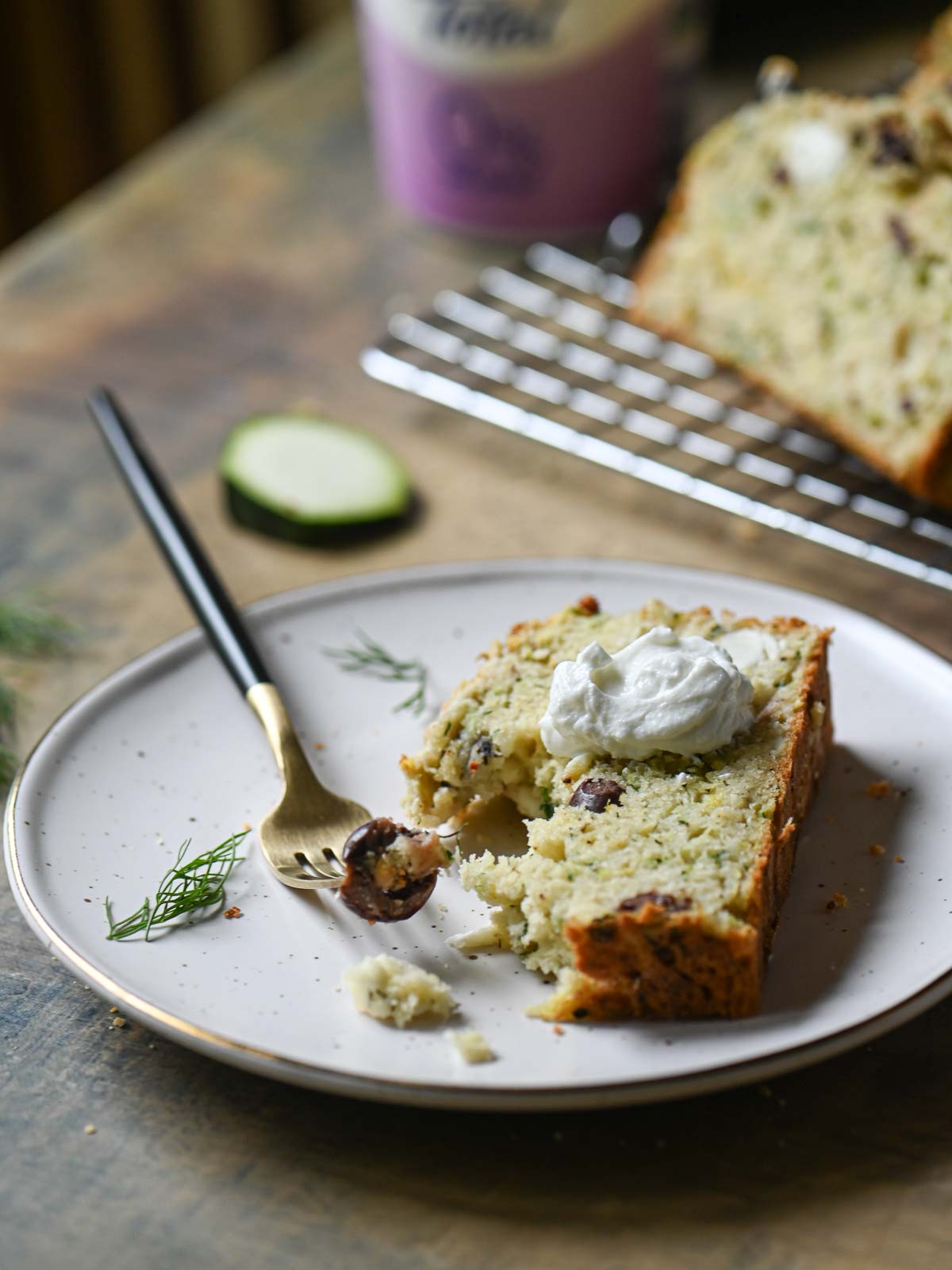 A serving of zucchini bread on a beige plate with yogurt and a fork to the left.