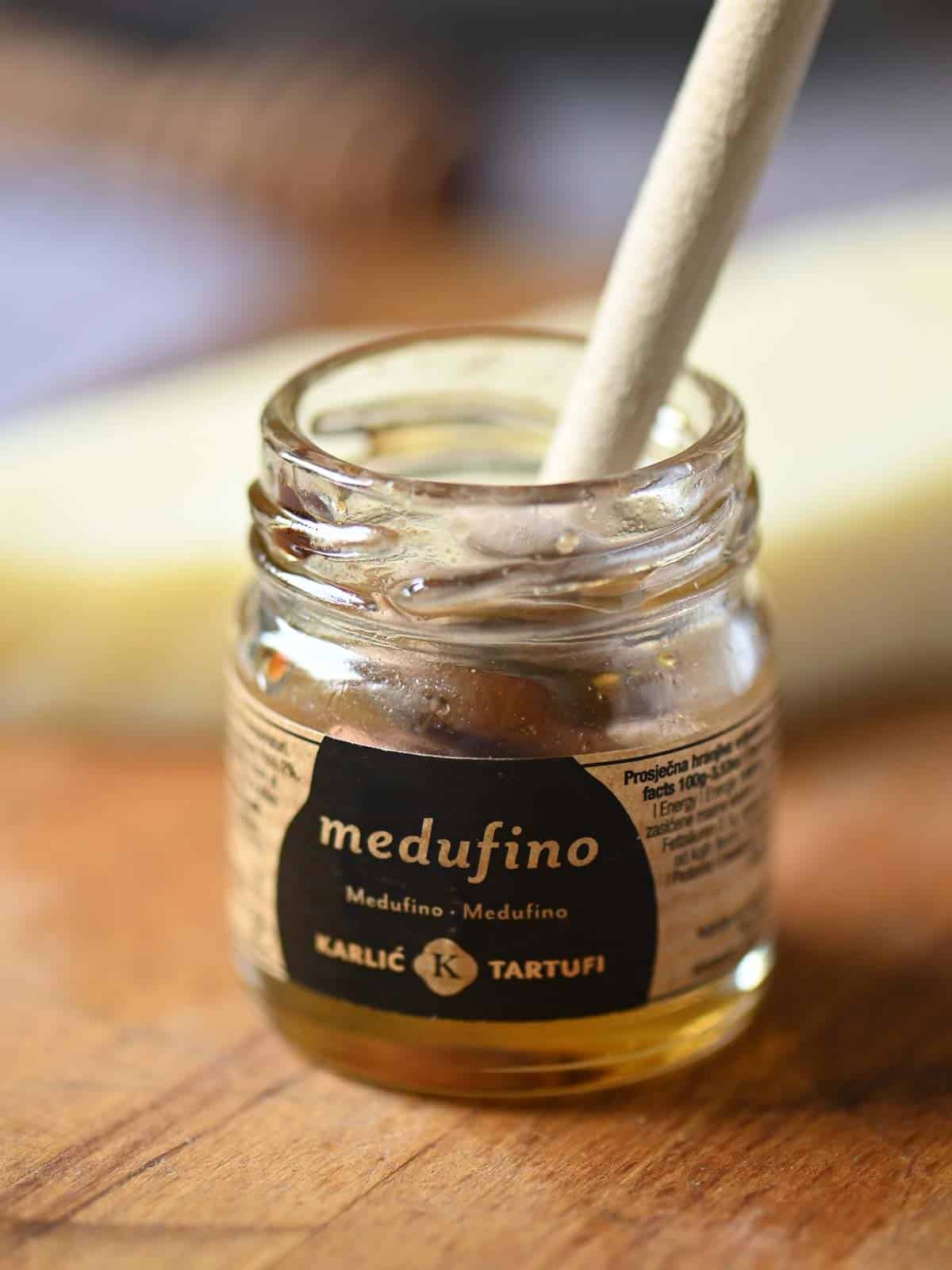 Medufino garlic tartufi in glass jar with spoon on wooden surface.