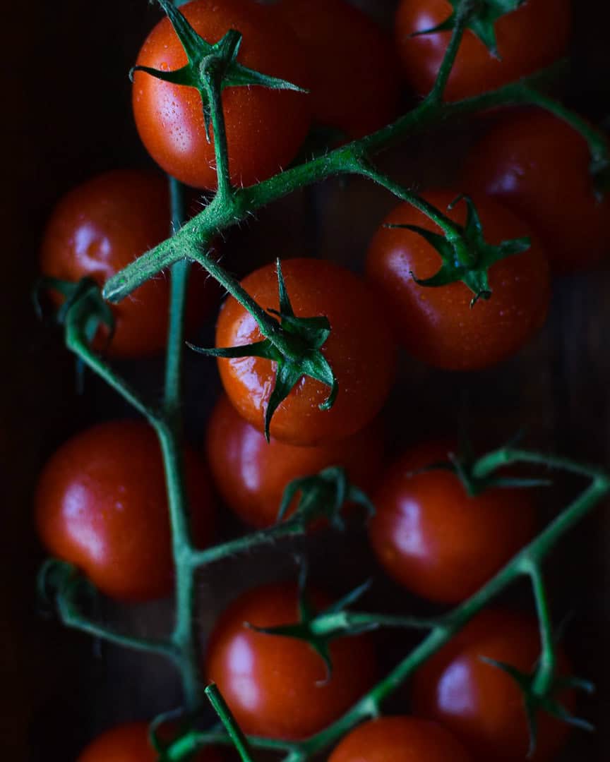 A dark and moody overhead shot of cherry tomatoes on the vine.