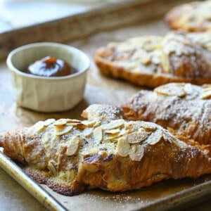 Almond croissants on a baking tray with apple butter to the left.