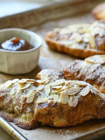 Almond croissants on a baking tray with apple butter to the left.
