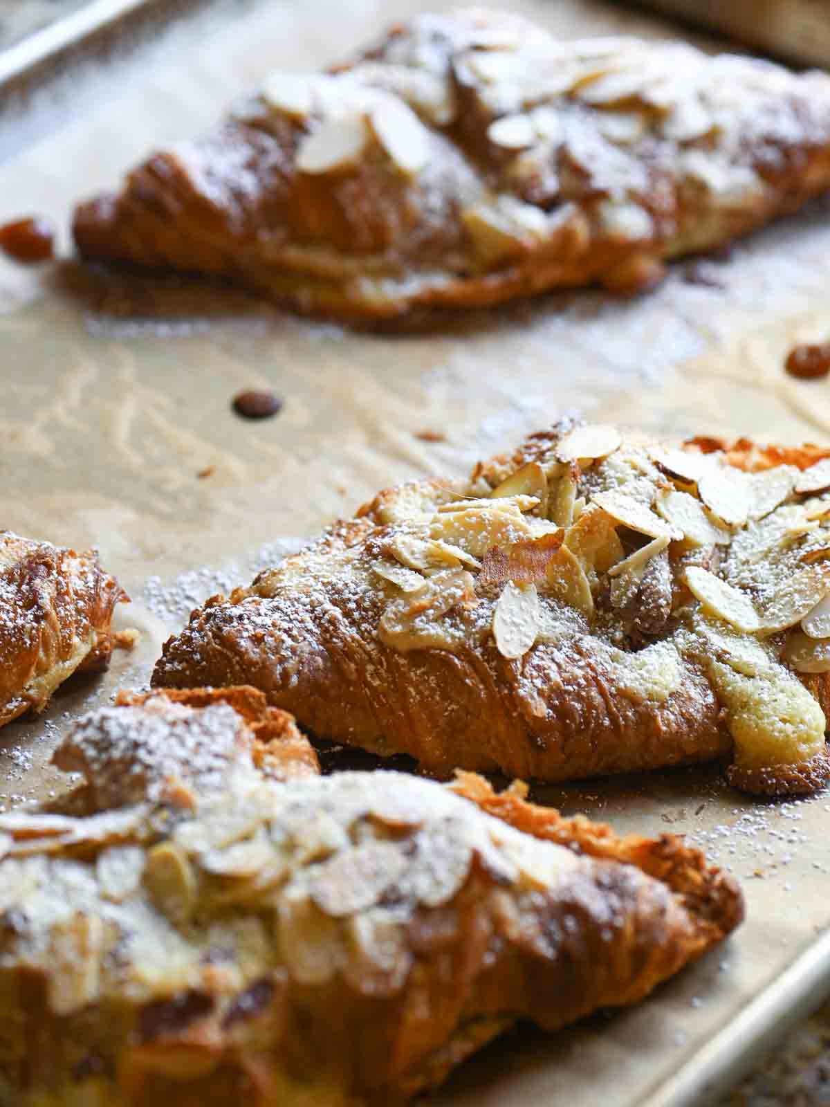 Close up of 3 almond croissants on a baking tray.