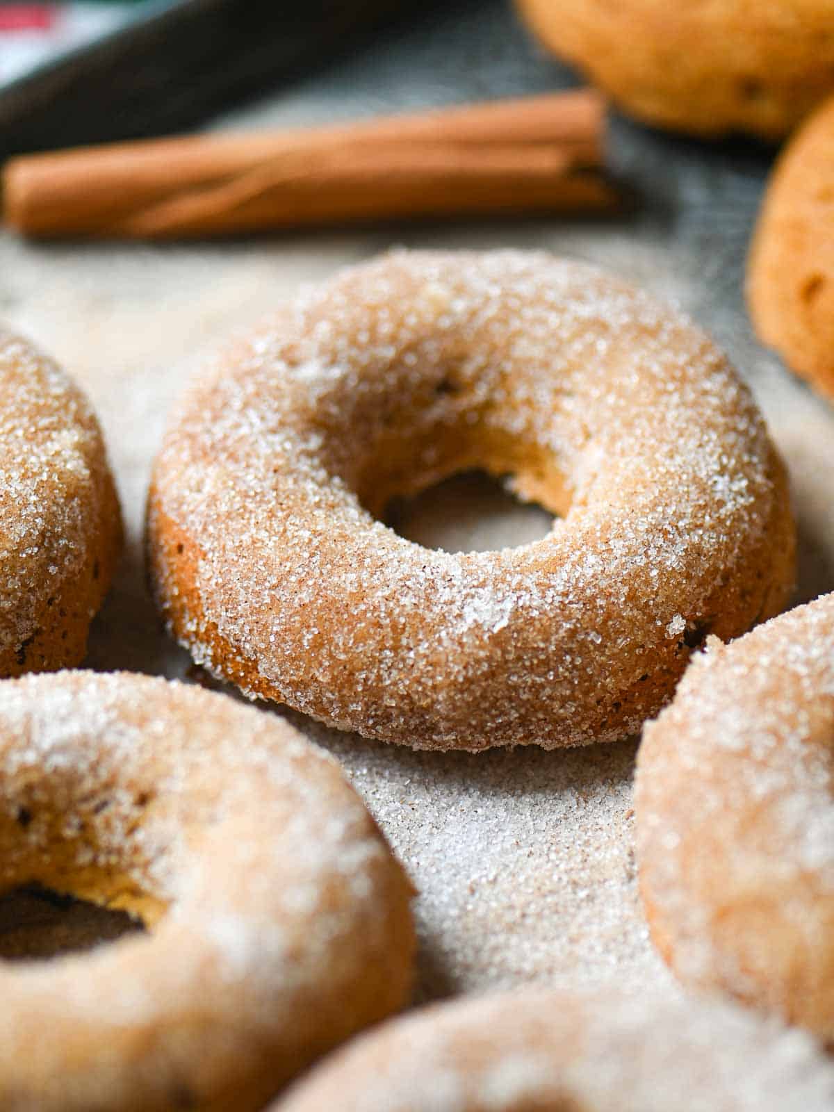 Close-up of a sugared apple donut on a tray with a cinnamon stick behind it.