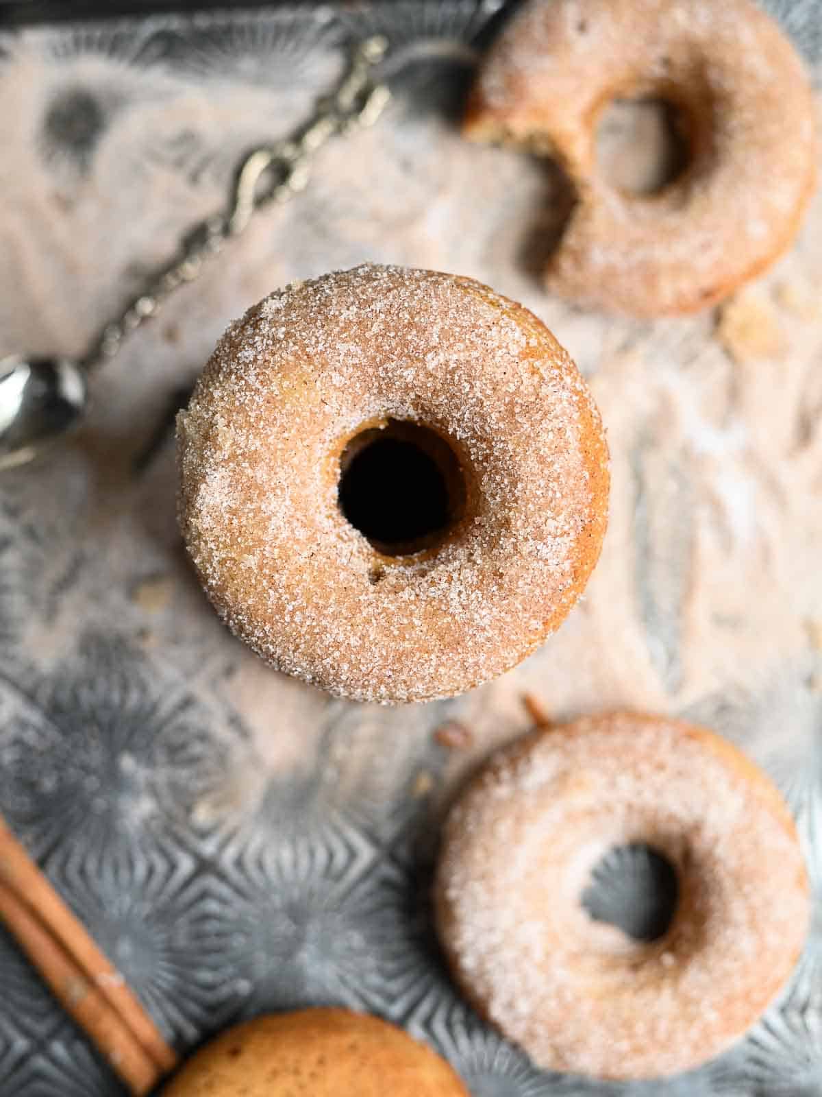 An overhead shot of apple donuts on a metal tray with sugar.