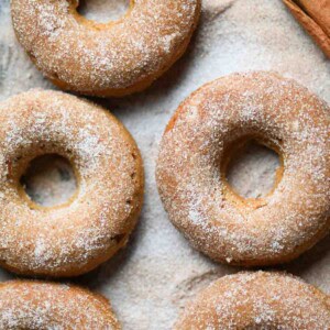 An overhead of sugared apple donuts with a cinnamon stick.