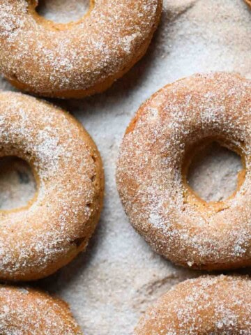An overhead of sugared apple donuts with a cinnamon stick.