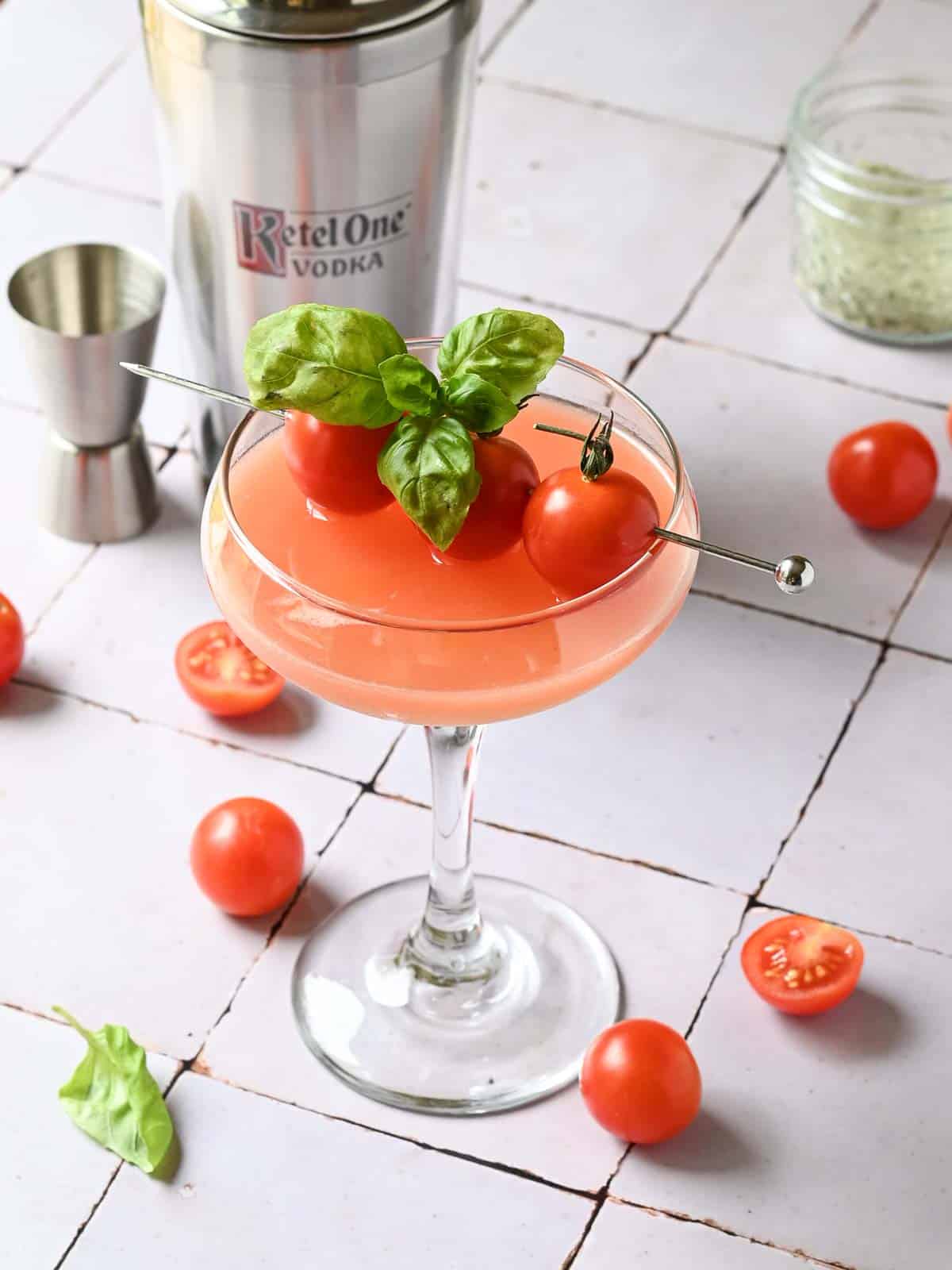 A tomato martini on a tiled surface with a cocktail shaker in the back.