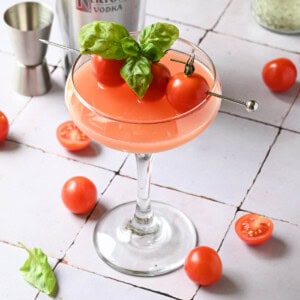 A close-up of a tomato martini on a tiled surface with tomatoes and basil.