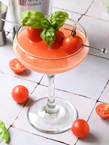 A close-up of a tomato martini on a tiled surface with tomatoes and basil.