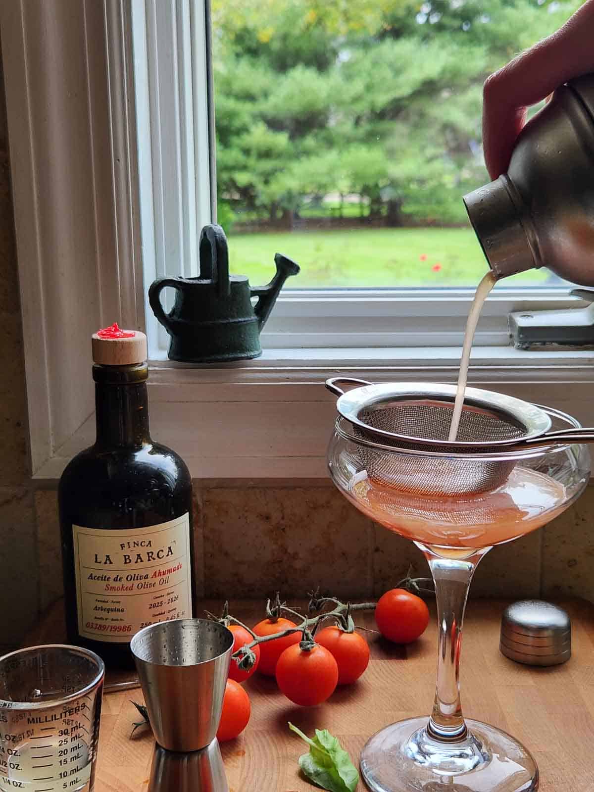 A hand pouring vodka through a strainer into a clear coupe glass.