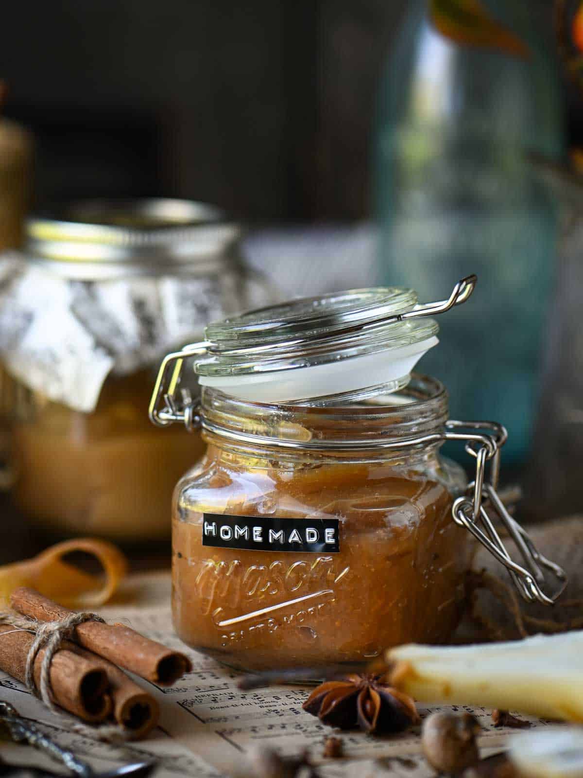 Homemade pear butter in a clear Mason jar with spices around it.