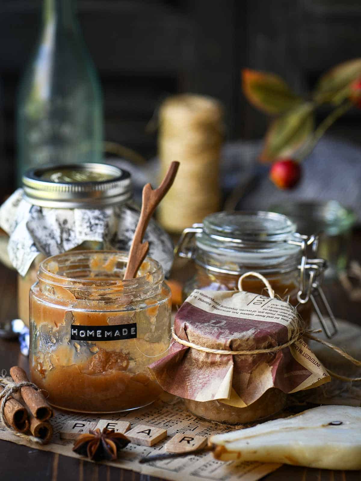 Four jars of pear butter in various sizes with spices and a sliced pear around it.