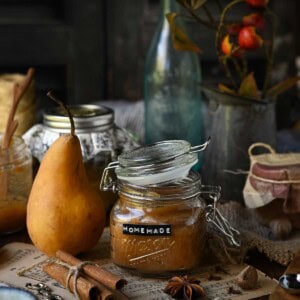Pear butter in a jar with a whole pear next to it surrounded by whole spices.