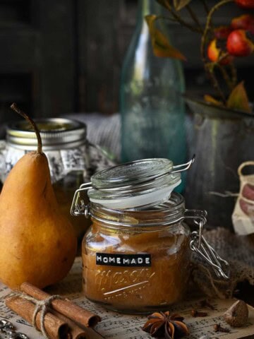 Pear butter in a jar with a whole pear next to it surrounded by whole spices.